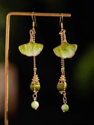 Close up of sage green ginkgo leaf tassel Chinese earrings with gold ear hooks, layered chains, and gradient green decorative beads