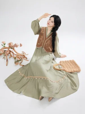 Side sitting view of sage green Chinese inspired maxi dress and brown embroidered vest set with decorative skirt hem