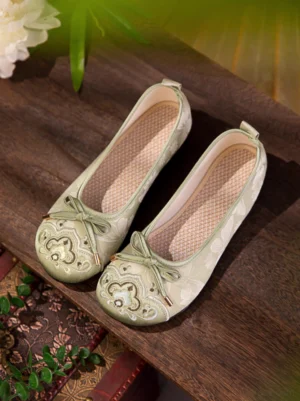 Sage green and off-white embroidered traditional Chinese Hanfu shoes displayed on a vintage wooden table with Ruyi toe embroidery, bow ornament, and woven breathable insole