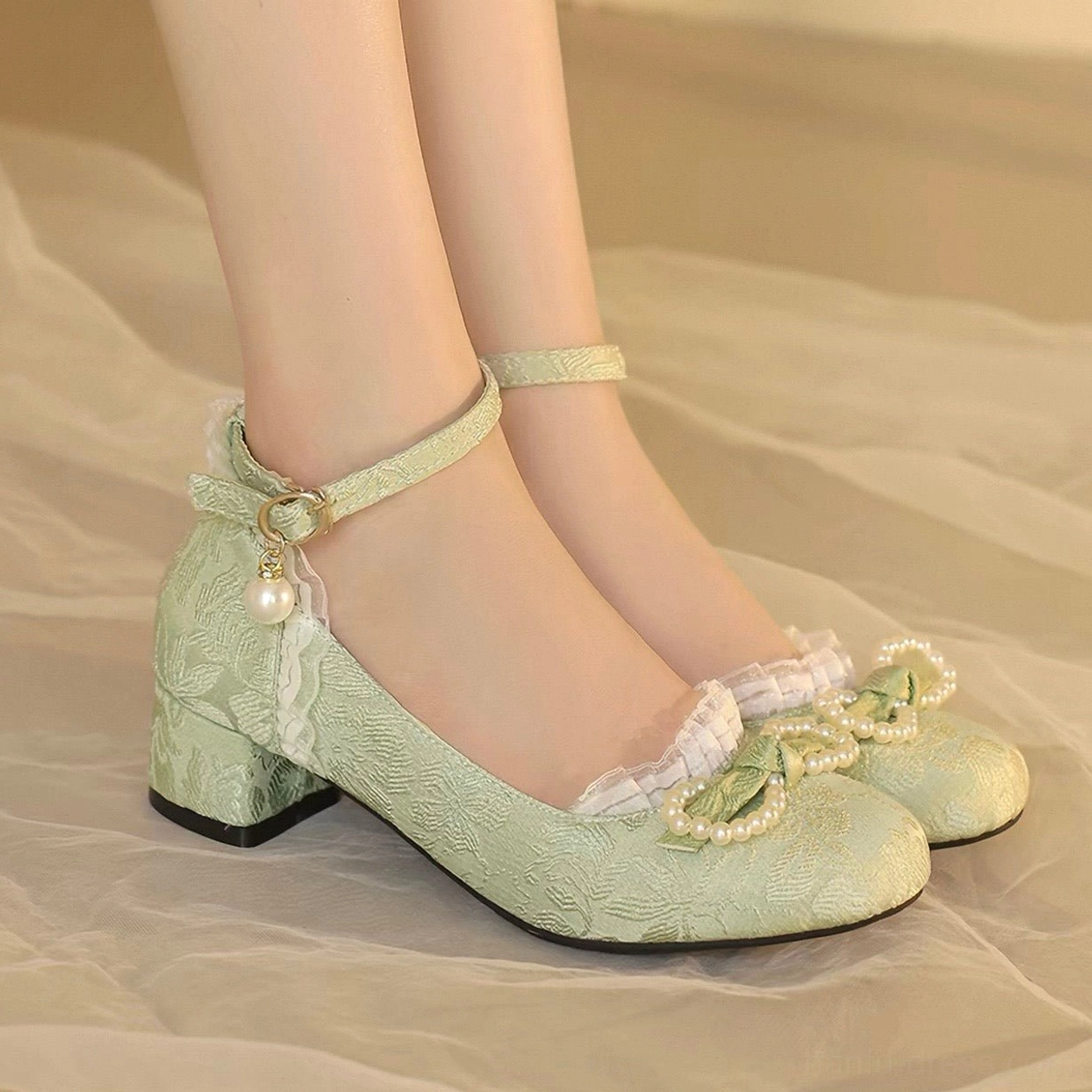 Sage green traditional Chinese Hanfu shoes with jacquard textile upper, pearl-studded bows, white lace trim, ankle strap, pearl pendant, round toe, and chunky block heel shown on foot