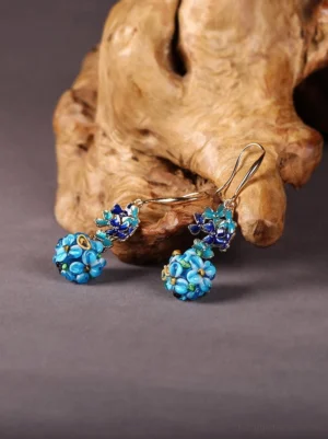 Sapphire blue floral beaded Chinese earrings displayed on a wooden decorative stand, showing layered blue flower clusters, gold-tone hooks, and vintage Oriental jewelry styling