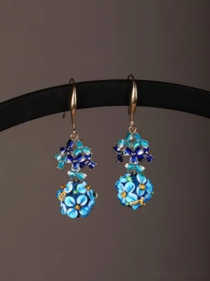 Front view of sapphire blue floral drop earrings hanging on a black display rod, featuring layered flower pendants and detailed blue enamel-style accents