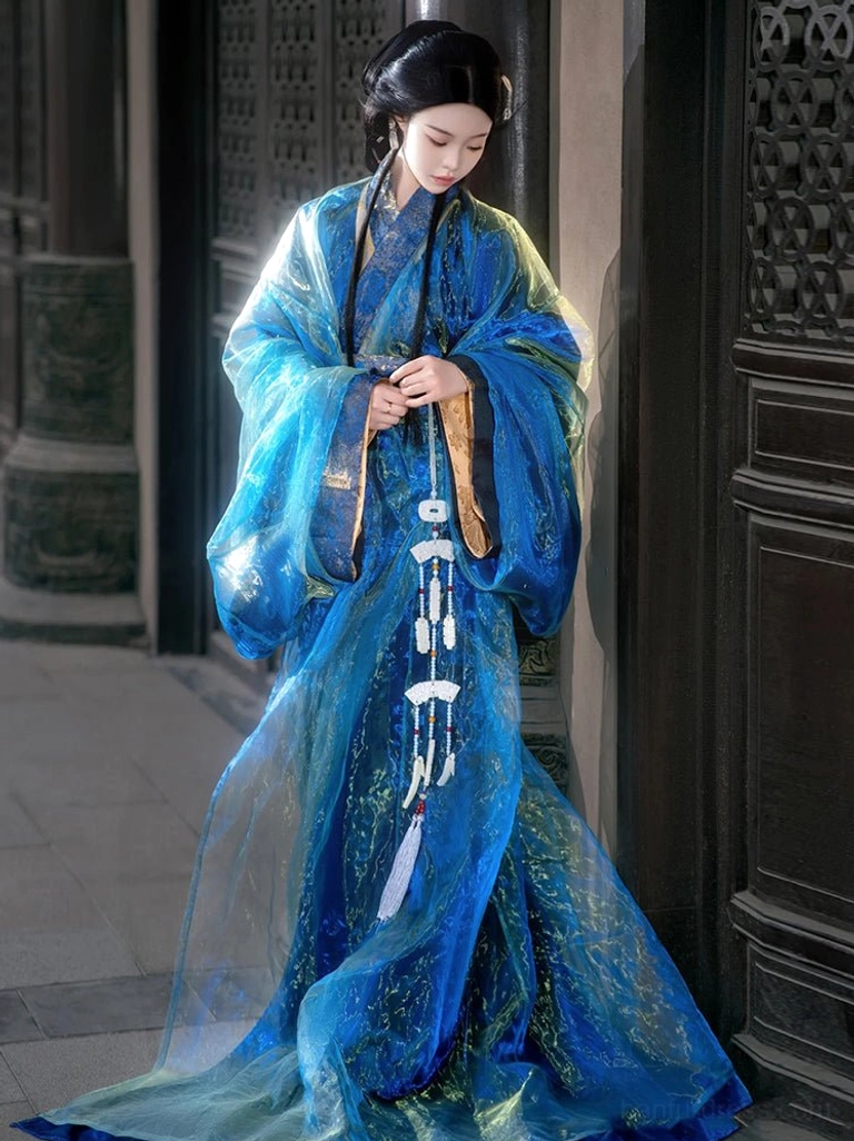Full-length side three-quarter view of a woman wearing a sapphire blue sheer floor-length Han Dynasty Hanfu gown with wide sleeves and elegant white tassel pendant decorations