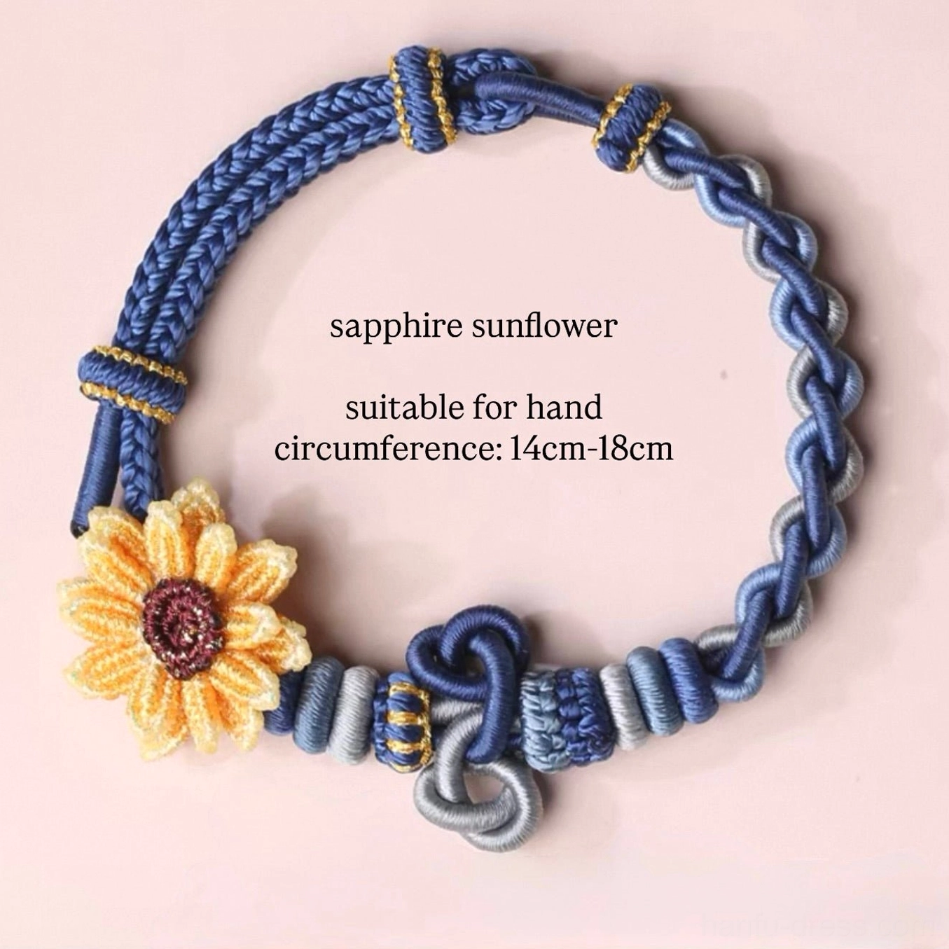 Sapphire sunflower handwoven Chinese knot bracelet with blue and light gray woven cords, golden accent knots, and yellow brown sunflower charm on a light pink background