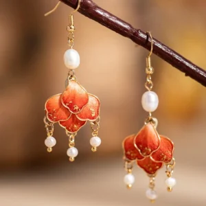 Scarlet floral tassel Chinese hook earrings hanging from a dark branch with red petals gold flecks and pearl-style bead drops