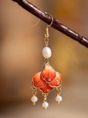 Close-up front view of a scarlet layered flower Chinese dangle earring with gold details top pearl accent and delicate tassels