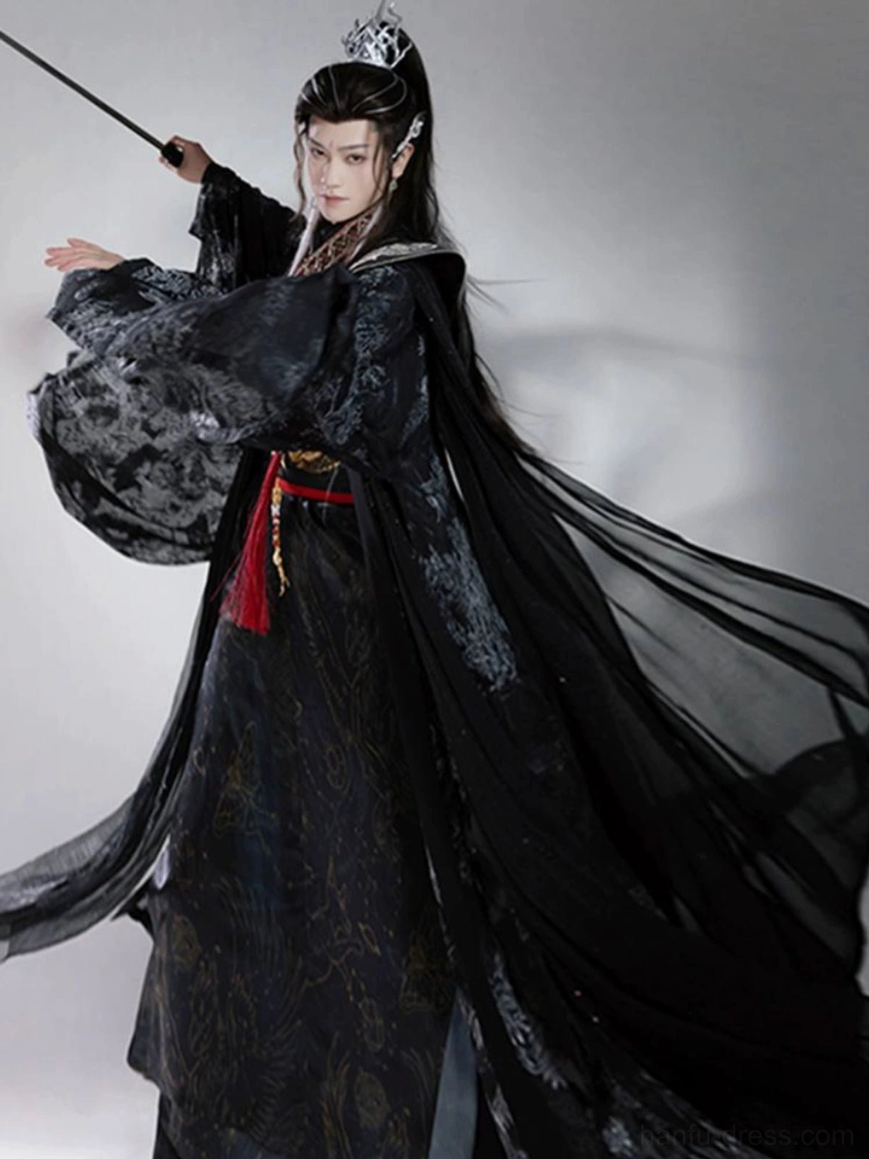 Men's dark Chinese fantasy Hanfu in dynamic martial arts pose showing the long flowing sheer black cloak, subtle pattern details, and red waist accessory