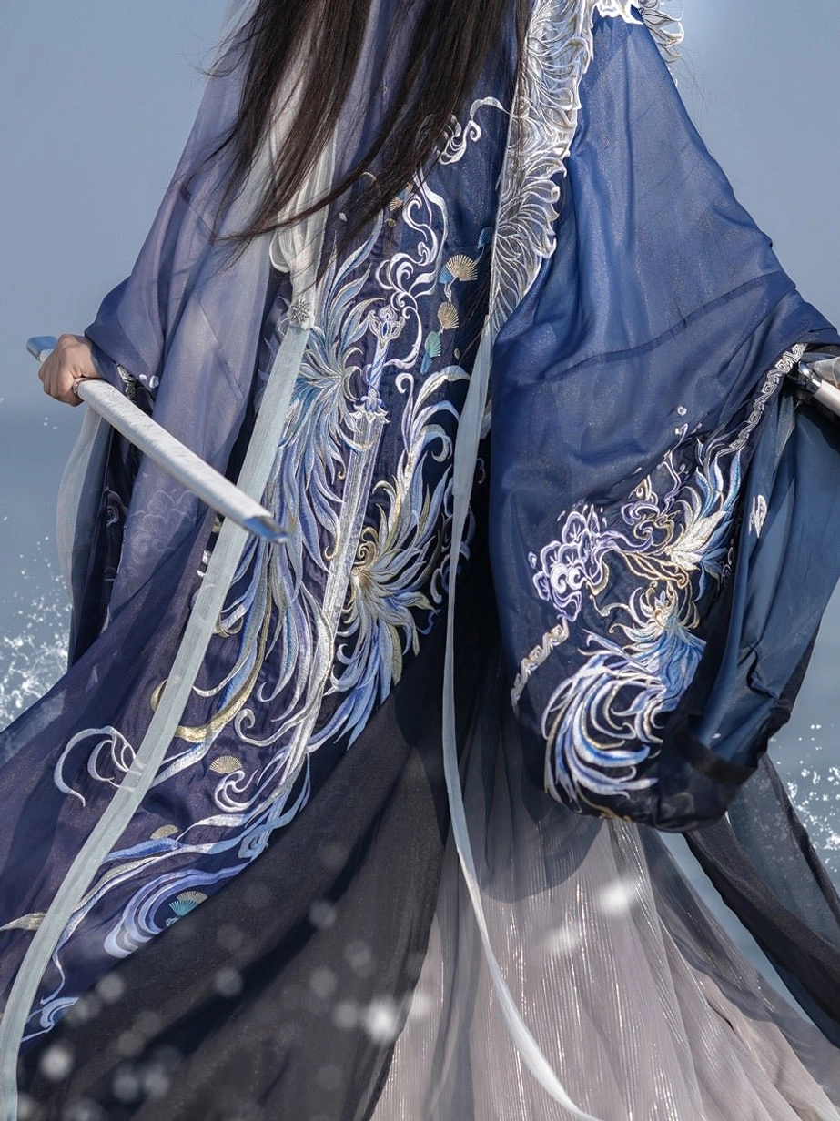 Close-up of silver gold phoenix embroidery on dark blue Shadowborne Blade hanfu fabric with sheer layers, light blue trim, and ceremonial sword handle