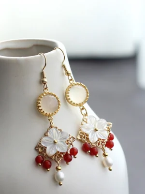 Chinese shell flower pearl drop earrings with red bead clusters and gold tone filigree displayed on a white ceramic vase