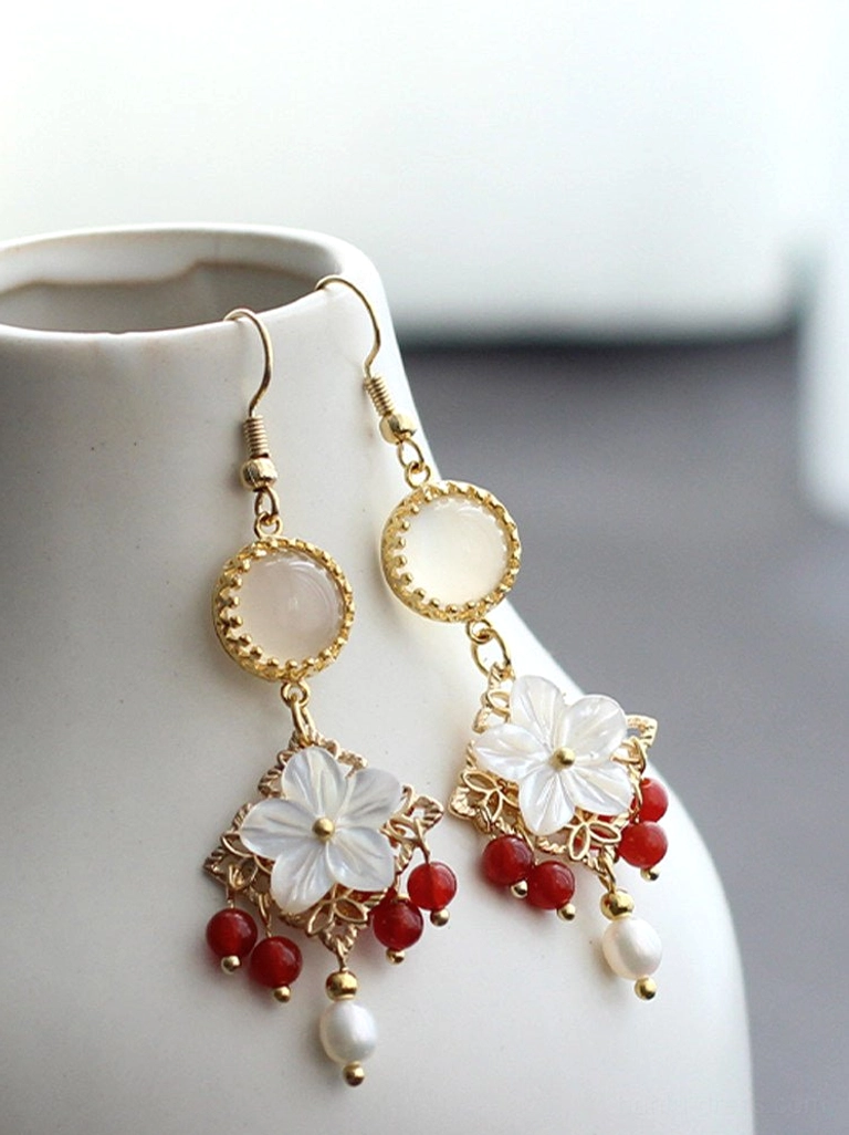 Chinese shell flower pearl drop earrings with red bead clusters and gold tone filigree displayed on a white ceramic vase