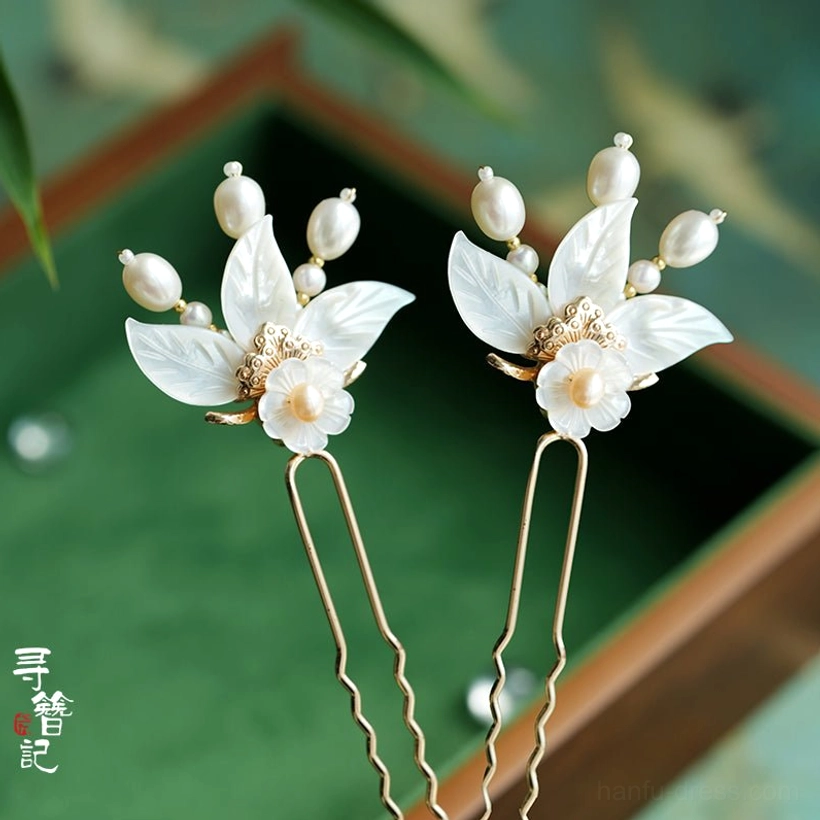 Pair of white shell leaf Hanfu hair pins with pearl accents and gold-tone wavy hair shafts displayed on a vintage green tray
