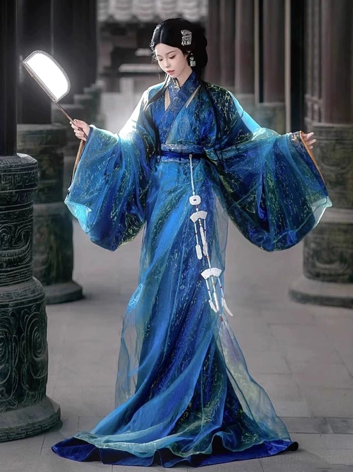 Full-length front view of a woman wearing a shimmering deep blue Han Dynasty straight-hem Hanfu robe with wide sleeves and neat white jade-style hanging tassels in a stone-columned courtyard