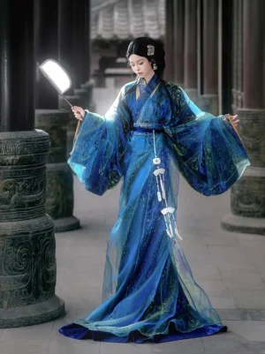 Full-length three-quarter view of a woman wearing a shimmering deep blue Warring States and Han Dynasty straight-hem Hanfu robe with wide flowing sleeves and white jade-style tassel ornaments in an ancient Chinese courtyard
