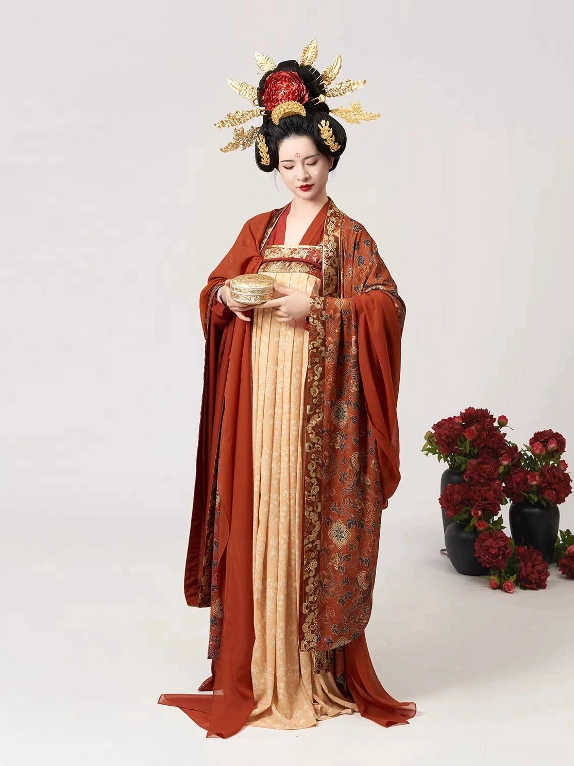 Full-body front view of a woman wearing the Shuangfengque Tang Dynasty Qixiong Ruqun Hanfu with an apricot-yellow patterned skirt, rust-red wide-sleeved cardigan, gold hair ornaments, and red peony decorations