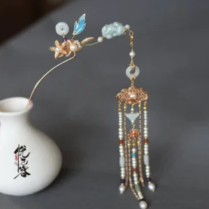 Si Yao Zhu Chinese tassel hair pin displayed on a white ceramic vase with gold-tone metal, blue enamel leaves, jade-like beads, freshwater pearls, and a flowing beaded tassel