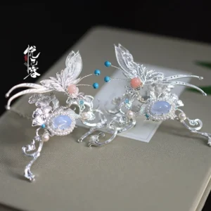 Silver crescent butterfly hanfu hair pin with openwork metal wings, blue agate accent, pink beads, and pearl details displayed on a tabletop