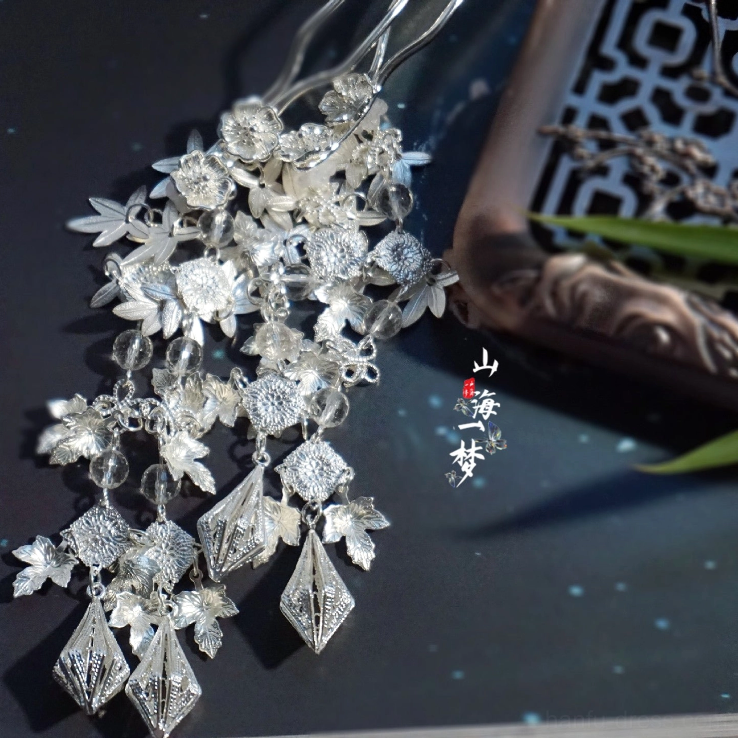 Flat lay display of a bright silver traditional Chinese hairpin with flower ornaments, rhombus pendants, and delicate tassel craftsmanship