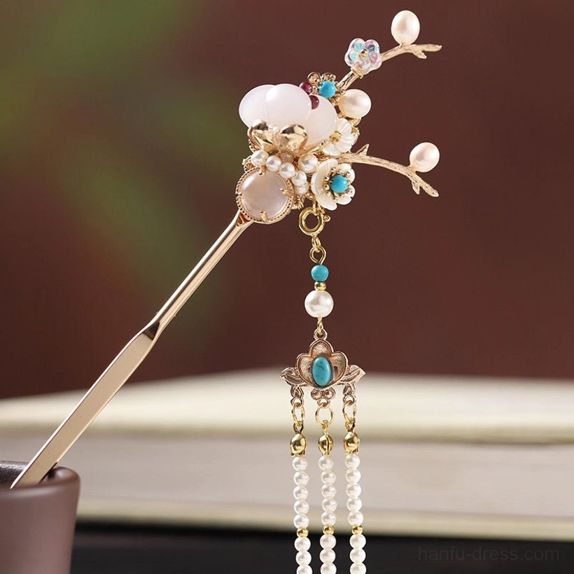 Single long Chinese hair stick shown from the front with an ornate golden flower branch top, milky white stones, blue decorations, and vintage pearl tassel
