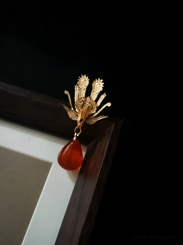 Side close-up of a single gold phoenix Hanfu drop earring with detailed filigree metalwork and ruby red teardrop pendant