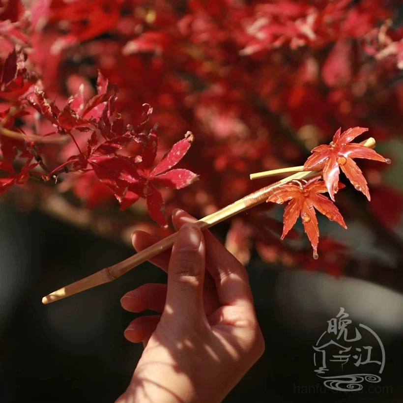 Single scarlet maple leaf Chinese hair stick held in hand against natural red maple foliage