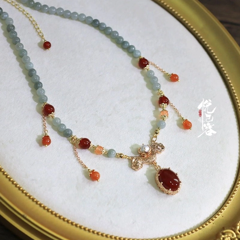 Single-strand Chinese-style Hanfu necklace with light blue jade-like beads, red agate beads, gold-tone details, oval red pendant, and dangling tassels on a velvet display tray
