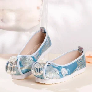 Sky blue embroidered Chinese Hanfu shoes with silver-white floral jacquard fabric, white trim, pearl-beaded tassels, beige lining, and thick white rubber soles displayed from a three-quarter top view
