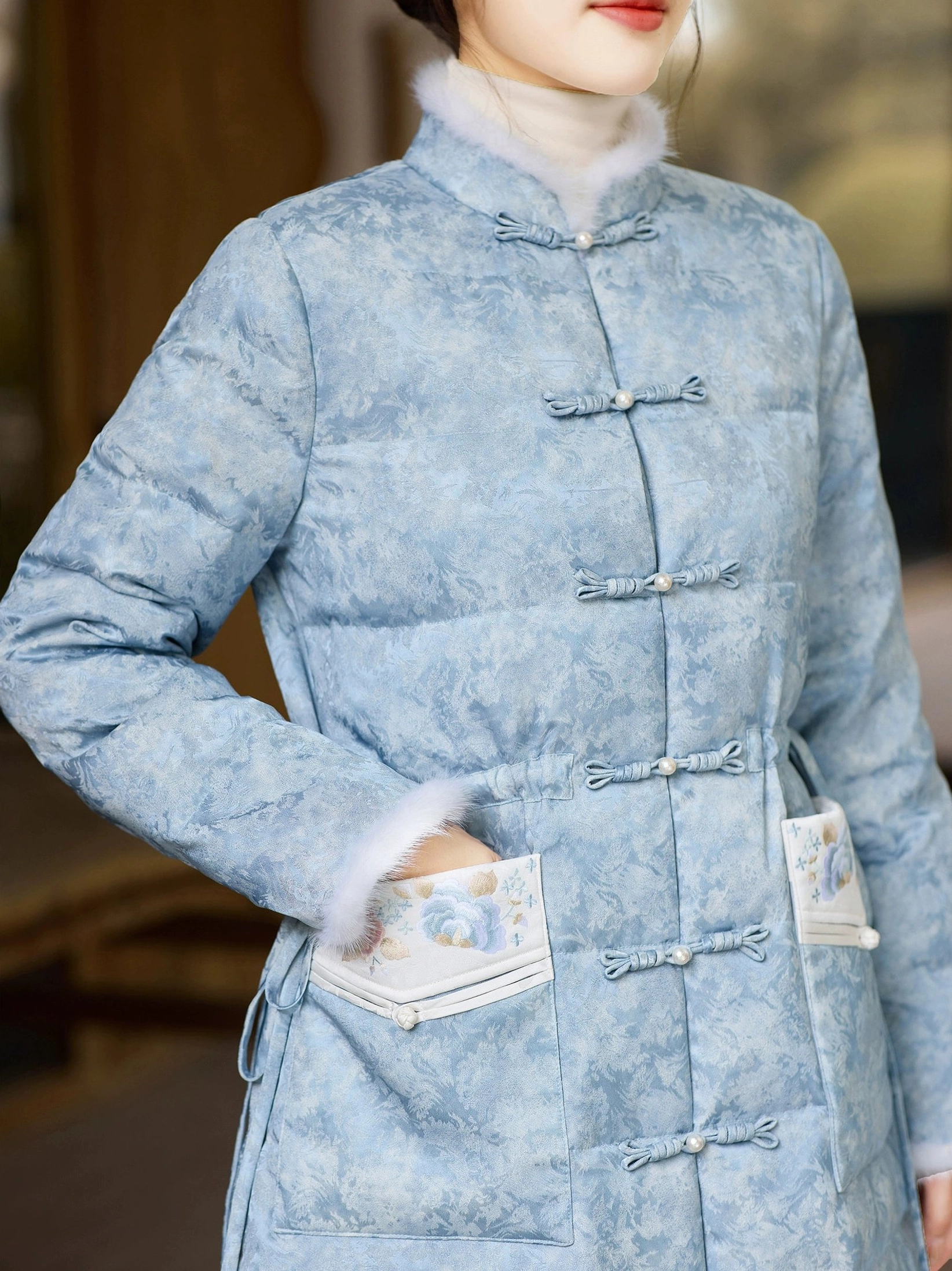 Close-up of sky blue qipao-inspired down coat showing traditional frog buttons plush stand collar embroidered pocket and adjustable waist detail