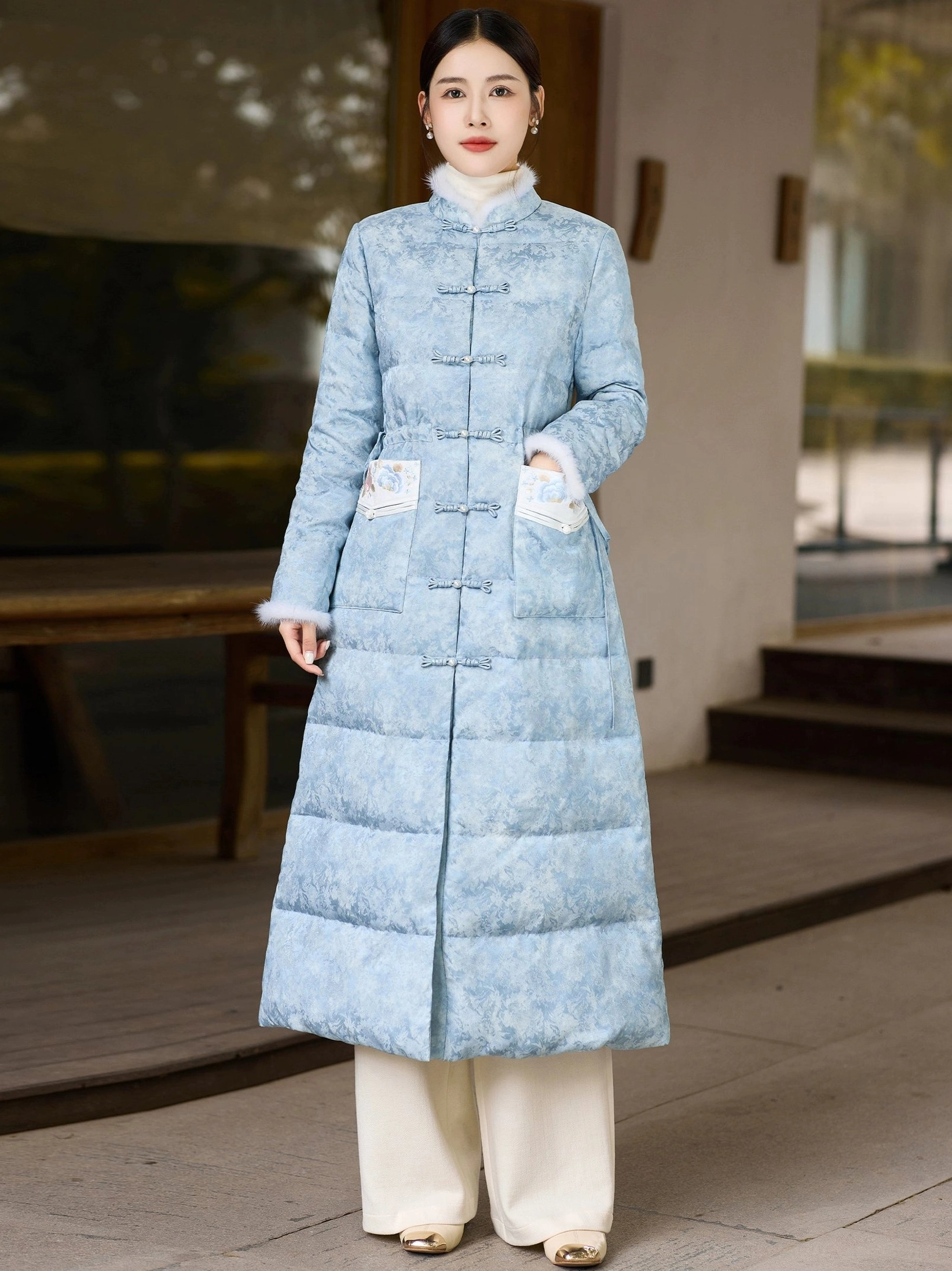 Full front view of women's sky blue qipao-inspired long down coat with frog buttons plush stand collar embroidered pockets and quilted Hanfu-style winter design