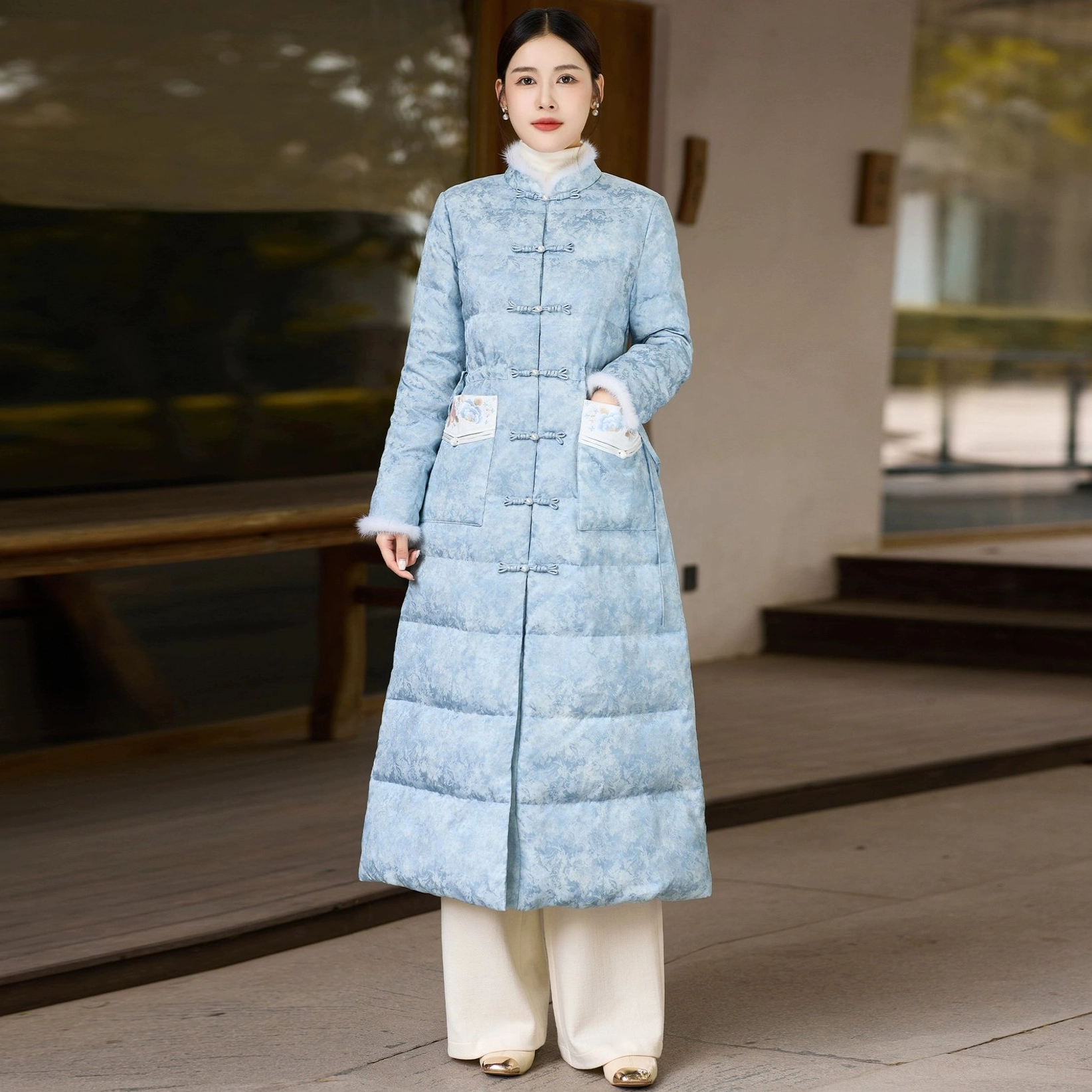 Full back view of women's sky blue long qipao-inspired down coat with quilted silhouette embroidered side pockets and plush trimmed cuffs