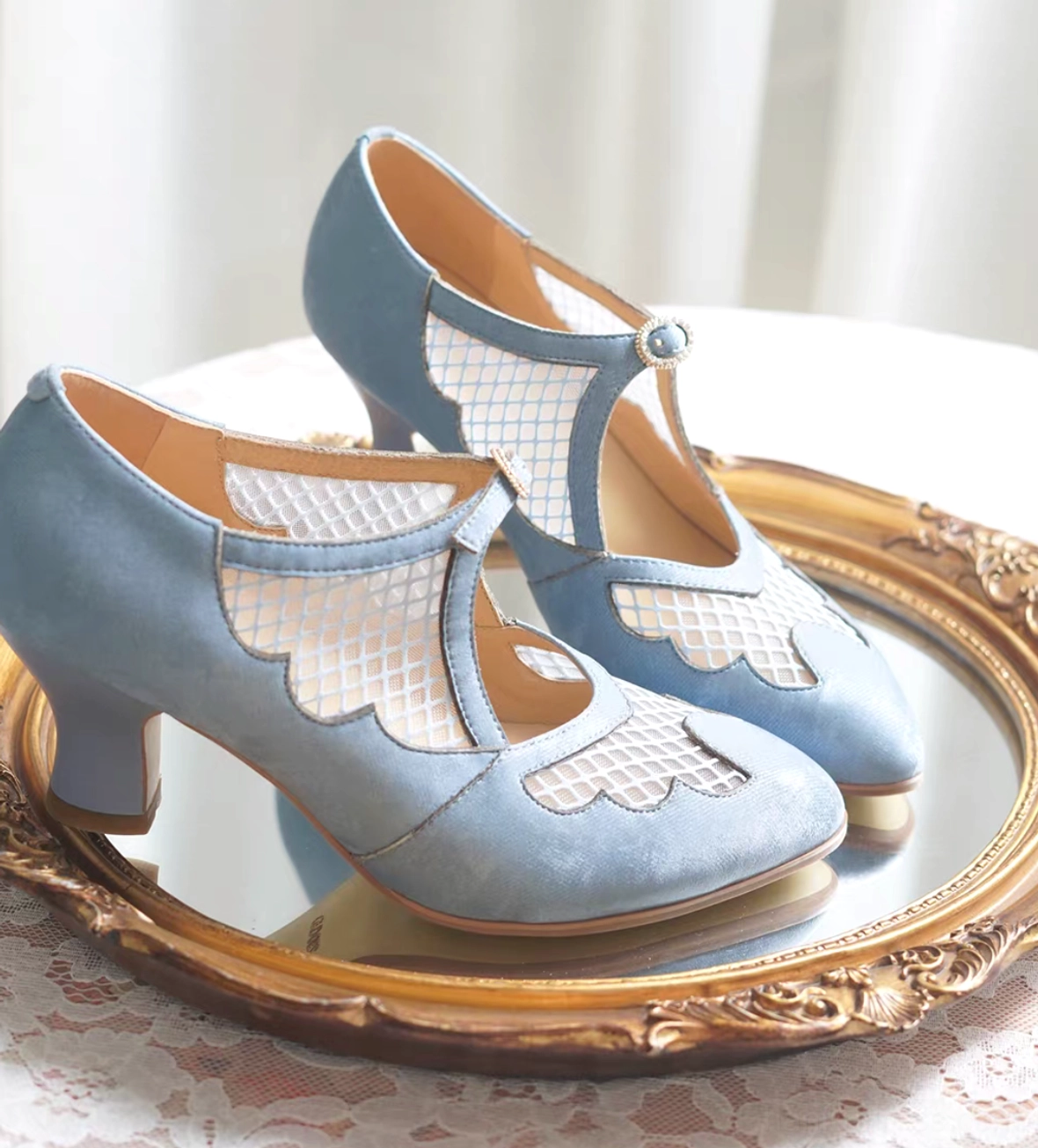 Sky blue vintage qipao Mary Jane heels with scalloped mesh vamp and T-strap buckle displayed on an antique gold rimmed mirror