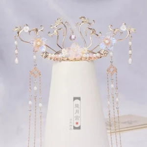 Sky Phoenix hanfu hair crown with gold toned metal vines, iridescent blue purple glass flowers, pearl drops, and long flowing tassels displayed on a white ceramic vase