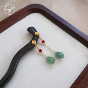 Close-up of Sleepless Flower traditional Chinese hair stick with polished dark wood shaft gold floral details red beads and green jade tassel pendants