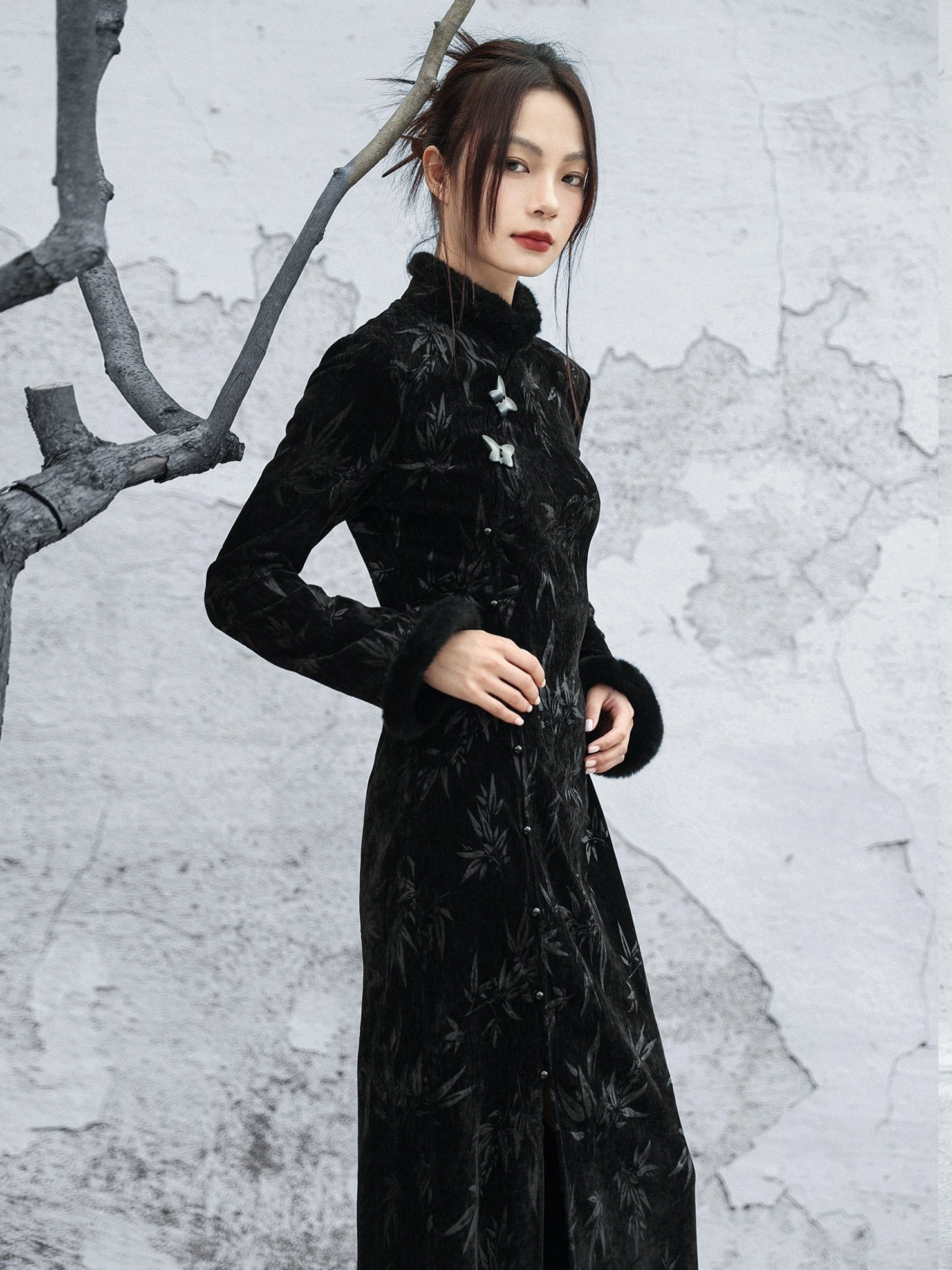 Slim-fit black bamboo print velvet cheongsam dress shown in a three-quarter standing view with fur-trimmed cuffs, stand collar, and frog buttons