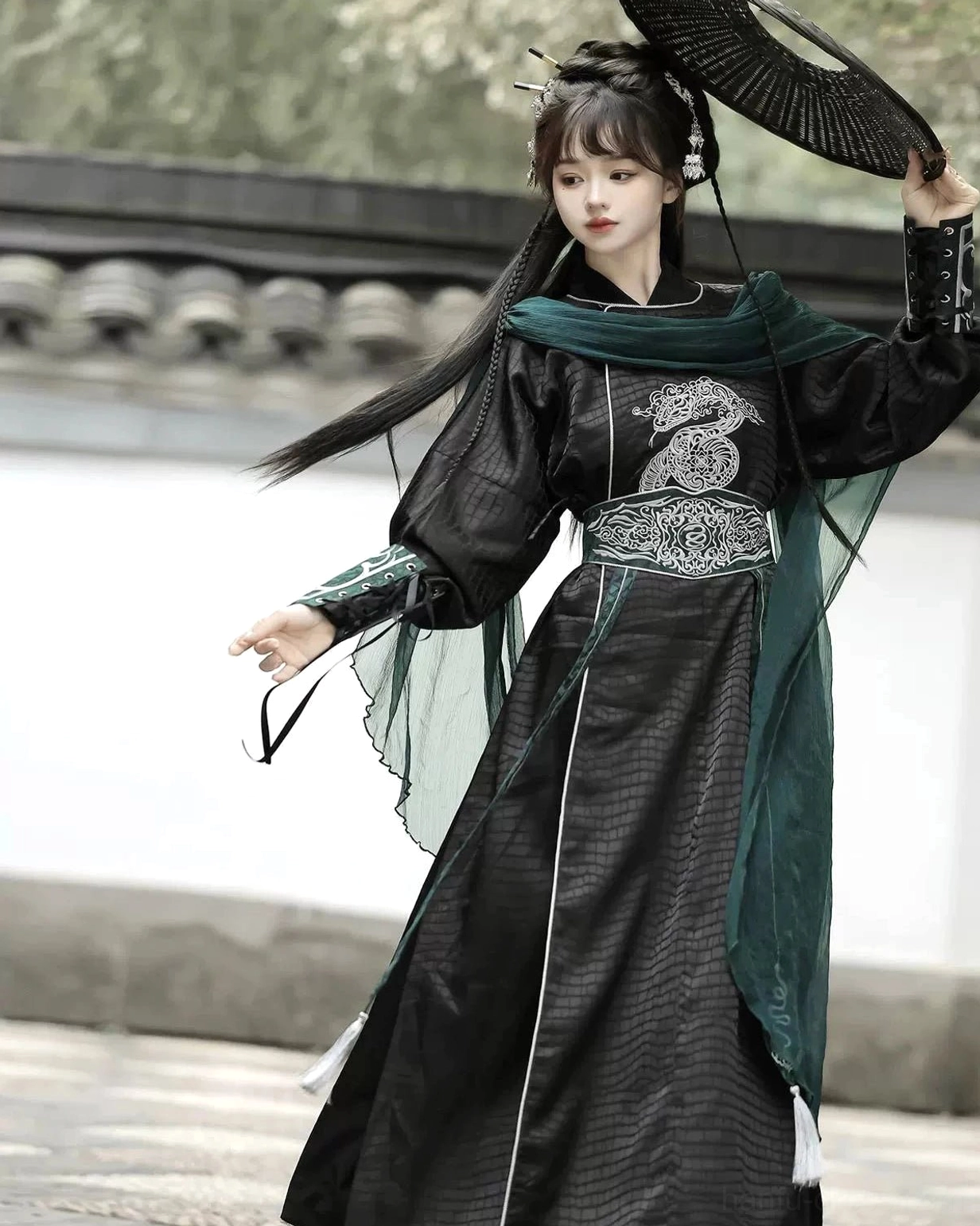 Side view of Snake Encounter modern Hanfu costume showing silver snake chest embroidery, dark green draped scarf, and flowing black robe in an ancient Chinese courtyard