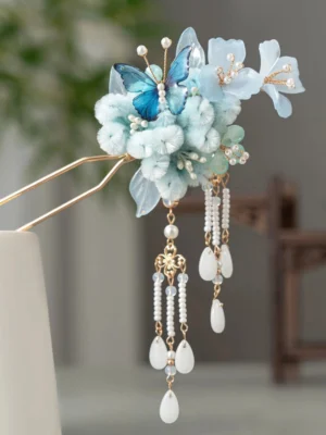 Front view of a traditional Chinese hair stick with light blue velvet flowers, blue butterfly ornaments, golden double prongs, pearl-style beads, and teardrop jade-style tassels