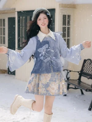 Dynamic front three-quarter view of a woman wearing the Snow Frost Cat modern Ming Hanfu set with dusty blue embroidered Bijia vest, flared sleeve blouse, floral mini Mamianqun skirt, beret, and beige boots in a snowy courtyard