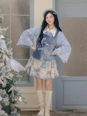 Full front view of the Snow Frost Cat modern Ming-style Hanfu outfit with square neck velvet Bijia vest, blue blouse, floral pleated Mamianqun horse face skirt, and knee-high boots beside a frosted Christmas tree