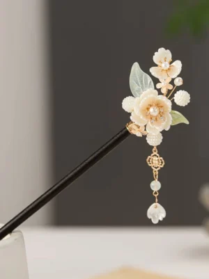 Close-up view of a snow hibiscus floral Chinese hair stick with a black wooden shaft, ivory flowers, pearl-style centers, green leaves, gold-tone fittings, and a layered tassel with cloud charm