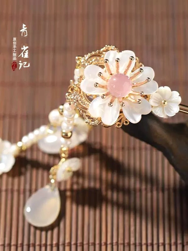 Close-up white shell flower ornament with pink center and gold-tone frame on Snow Lyrics traditional Chinese hair stick