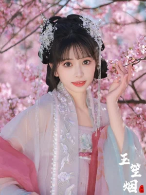 Snowy crystal flower Hanfu hair accessories set with two silver-white tassel hairpins styled with embroidered pink and blue traditional Chinese clothing in a cherry blossom garden