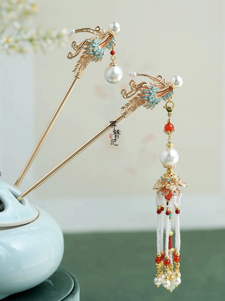 Side view of a Soaring Dragon Chinese hairpin with a gold-tone body, blue cloisonne-style dragon head, white pearls, red beads, and layered hanging tassel decorations