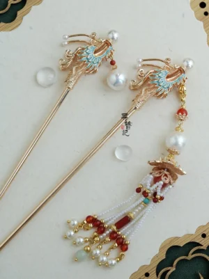 Top view of a Soaring Dragon Chinese Hanfu hairpin with a blue enamel dragon motif, gold-tone metal frame, white pearl beads, red agate-style accents, turquoise beads, and a long layered tassel