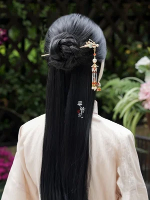 Woman wearing a Soaring Dragon traditional Chinese hairpin in a low black hair bun with a flowing beaded tassel, styled with a light pink Hanfu top in a garden