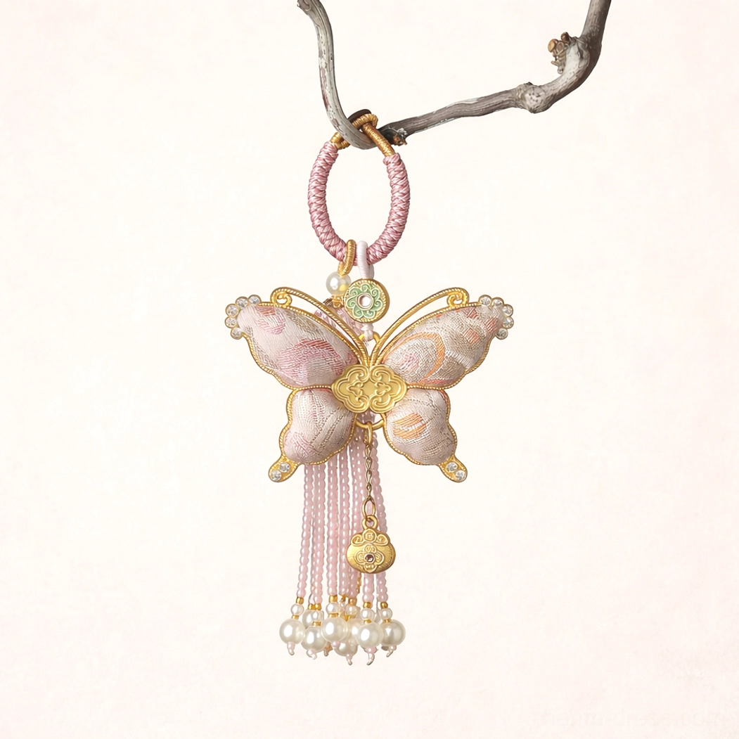 Pastel pink Song brocade butterfly Chinese keychain and handbag charm with braided loop, pearl-like bead tassel, gold-toned ornaments, and decorative pendants hanging from a tree branch