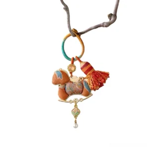 Song brocade rocking horse Chinese keychain bag charm with red tassel, pearl-like pendant, colorful beads and gold-tone hardware hanging on a twig