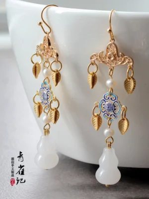 Vintage Chinese lantern earrings with gilded filigree enamel longevity charm pearl accents leaf pendants and white gourd-shaped drops against a white ceramic bowl