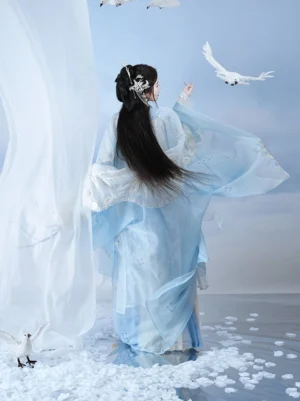Back view of a flowing light-blue Song Dynasty style Hanfu qiyao ruqun dress with sheer layers, long black hair, traditional hair ornaments, and floating white petals