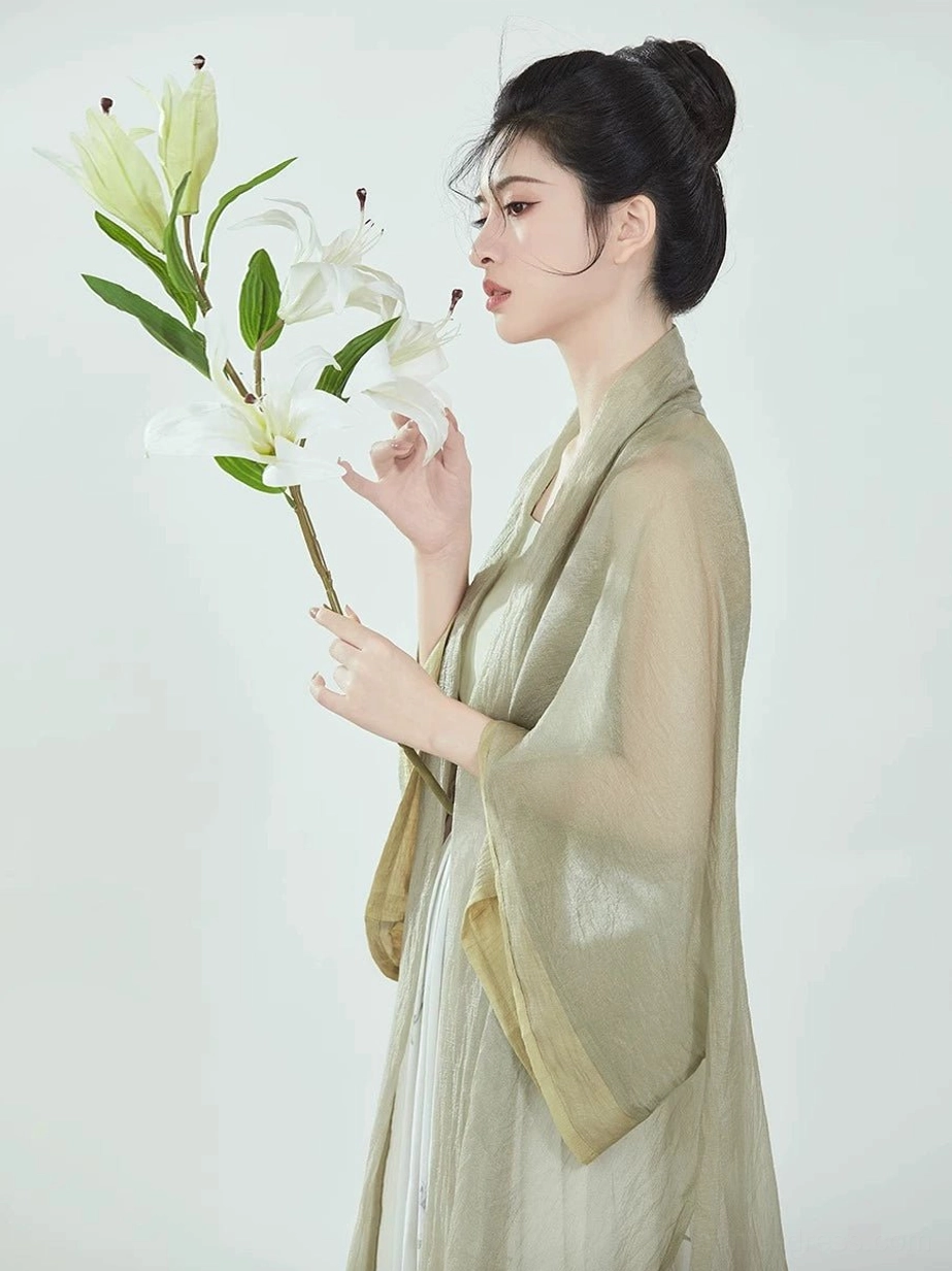 Close-up side profile of a woman wearing a sage green modern Chinese Hanfu overcoat with wide sleeves, soft drape, and elegant layered styling