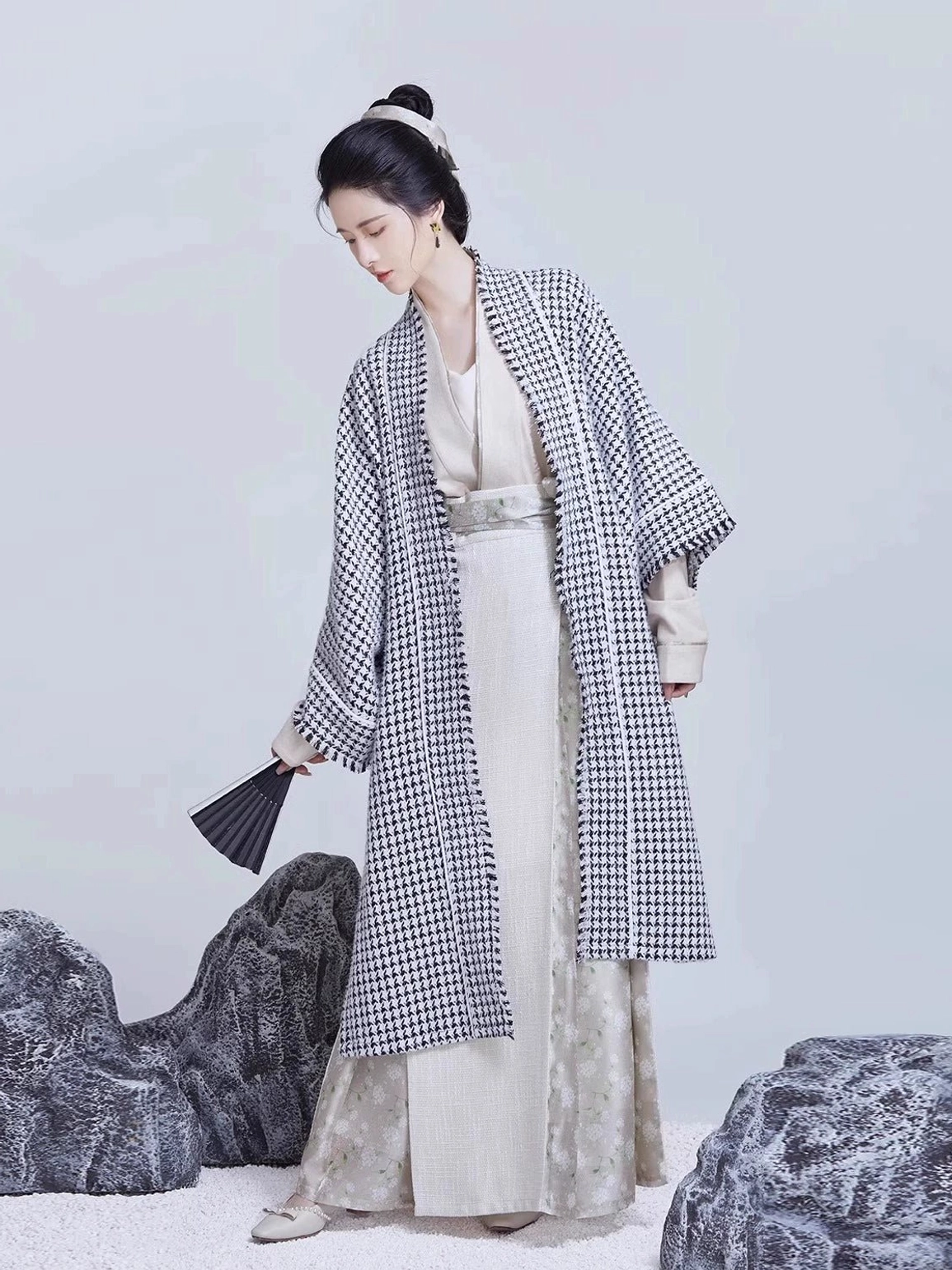 Song Dynasty modern Hanfu set with houndstooth beizi jacket, off-white inner top, three-pleat wrap skirt, wide sleeves, and black folding fan in a minimalist Chinese-style studio