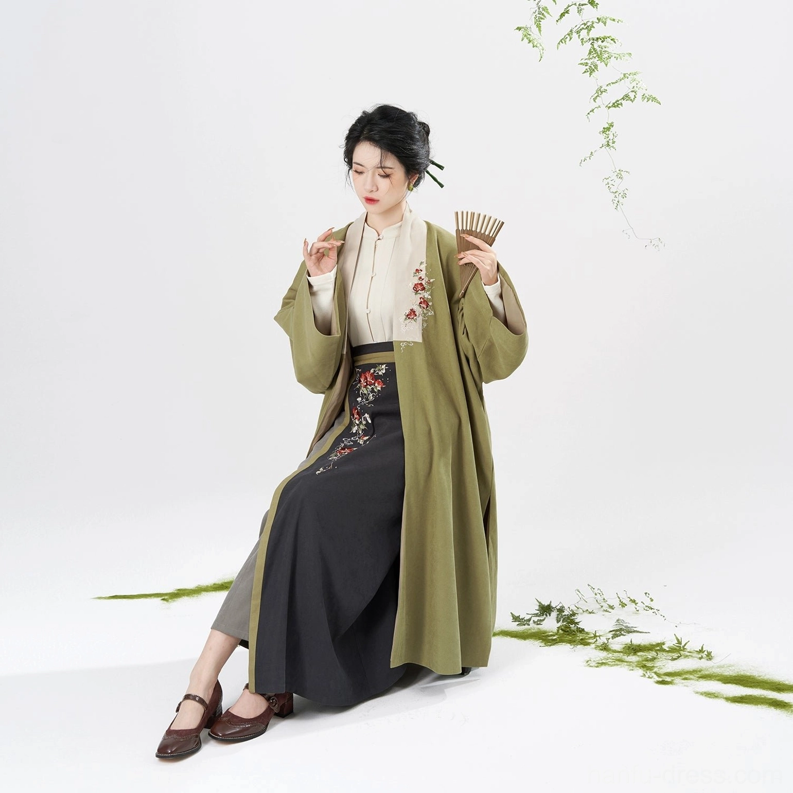 Seated model in embroidered Song Dynasty modern hanfu full set with olive green coat dark grey skirt and folding fan